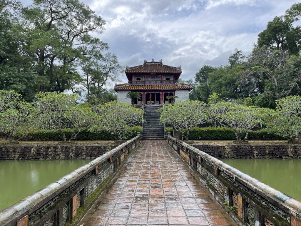 Visiter Hué au Vietnam : que faire & conseils pratiques Vue sur un des édifices du tombeau du roi Minh Mang avec pont et lac